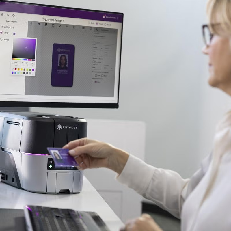 ID Card Software & Instant ID Support | ID CardSolutions - Person swiping a purple ID card into an Entrust card printer while a monitor on the desk shows design software. ID Card Software & Instant ID Support | ID CardSolutions - Person swiping a purple ID card into an Entrust card printer while a monitor on the desk shows design software.